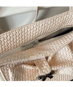 Detail of metal zipper closure and black bow charm on beige woven tote bag