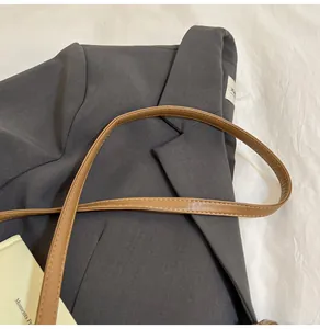 Mise à plat d'un sac seau en cuir marron associé à un blazer gris foncé texturé