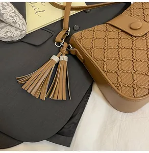 Détail du sac bandoulière marron en cuir tressé avec pompons ornés de strass brillants