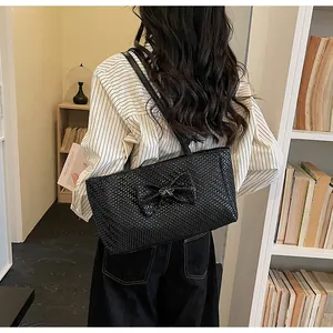 Detail of a black woven tote bag with a large bow and silver butterfly buckle on a shoulder strap
