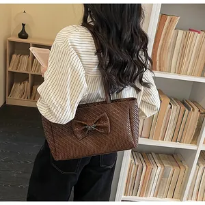 Detail of dark brown woven tote bag with bow accent and books in background