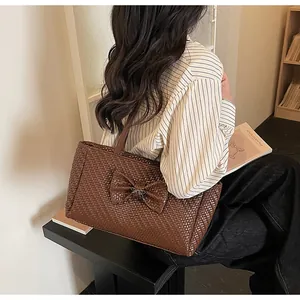 Detailed view of dark brown woven tote bag with large leather bow and metal ornament