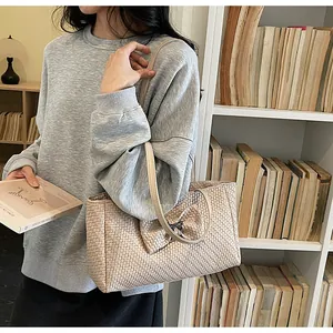 Detail of beige woven tote bag with large bow and metal accent on a female model