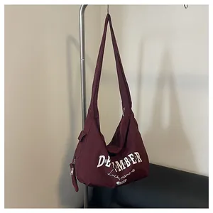 Detail der weinroten Nylontasche mit weißem Retro-Schriftzug und seitlicher Reißverschlusstasche