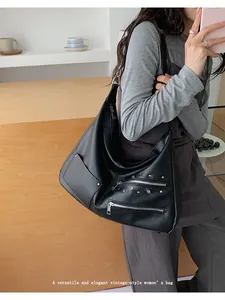 Close-up of vintage black hobo bag with silver rivets and zippers on a person