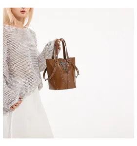 Detail of brown glossy leather bucket bag featuring metal rivets and a cross sword pendant