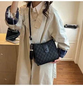 Détail d'un sac seau tressé noir avec pompon et fermoir magnétique sur un trench-coat beige