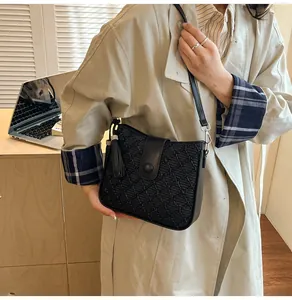 Détail du sac seau noir avec motif texturé et gland décoratif sur un trench beige