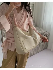 Detail of a beige leather hobo bag with silver rivets and large front pocket on a model