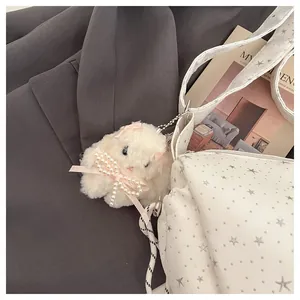 Close-up of white plush bunny charm with pink ribbon bow on a stylish white tote bag