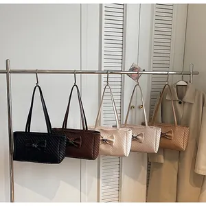 Row of five colorful woven tote bags with 3D bow detail hanging in a minimalist room