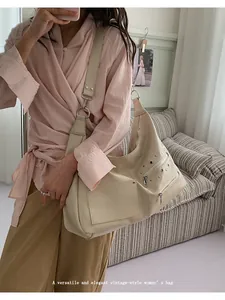 Detail of cream beige hobo bag with matte leather, zippers, and rivets on striped sofa