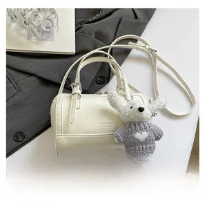 Detail of white cylinder Boston bag with rabbit plush charm and size comparison to phone
