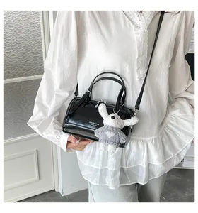 Detail of black glossy Boston bag with cute plush bunny pendant and leather handle