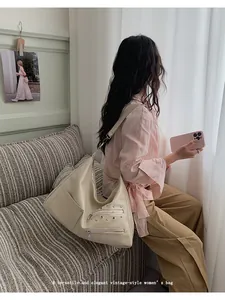 Detail of cream hobo bag with silver studs and multiple zipper pockets on model