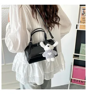 Detail of black glossy Boston bag with plush bunny charm worn by model in white blouse