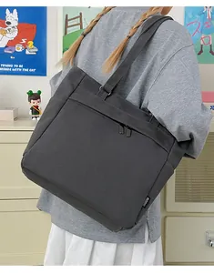 Detail of dark grey canvas tote bag showing front zipper pocket and woven brand label