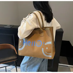 Close-up of brown canvas tote bag with blue Hello text and smiley face on model
