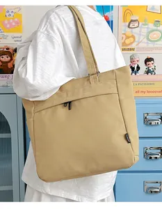 Khaki canvas tote bag with front zipper pocket and side logo tag shown on shoulder