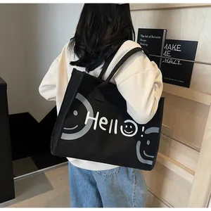 Rear view of a model wearing a black large canvas tote bag with a white Hello smile design
