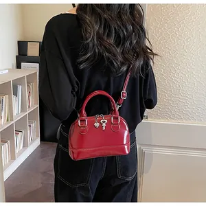 Detail of red patent leather shell bag with silver heart charm on model in home setting