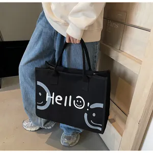 Detail of black canvas tote bag showing white Hello text and smiley face print