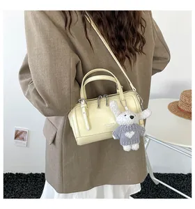 Detail of light yellow Boston bag with dual handles and a cute rabbit plush charm