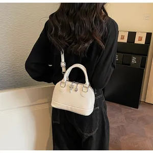 Detail of white shell handbag featuring silver heart-key charm and slim shoulder strap
