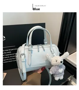 Detail view of a blue barrel bag with double handles and a cute poodle plush charm accessory
