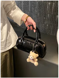 Gros plan du sac Boston en cuir verni noir avec quincaillerie dorée et pendentif ours