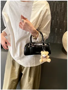 Détail du sac à main en cuir verni noir avec quincaillerie dorée et breloque ours