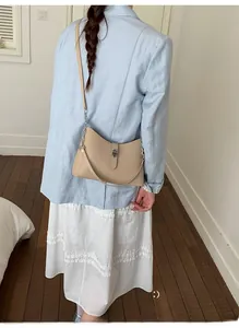 Detailed view of beige shoulder bag with silver buckle worn with a light blue blazer