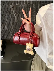 Détail du sac cylindre bordeaux en cuir ciré avec un joli pendentif en ours en peluche