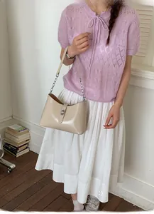 Detail of creamy beige saddle bag with silver twist lock and chain strap on light outfit