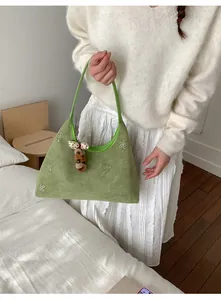 Dettaglio borsa a spalla in camoscio verde con texture floreale e ciondolo a fungo