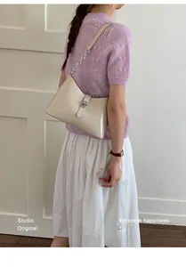 Detail of minimalist cream leather underarm bag featuring a metallic turn-lock closure