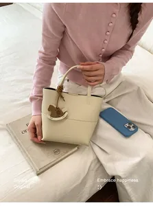 Detail of off-white leather bucket bag featuring a brown horse charm and textured finish