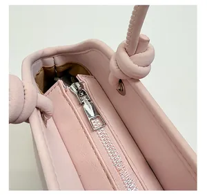 Close-up of pink leather handbag showing silver metal zipper and knotted strap detail