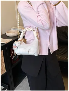 Detail of creamy white pleated handbag with gold chain strap and cute cat charm