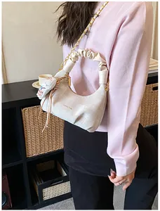 Detail of a chic cream dumpling bag with ruched handle, gold chain, and cat charm pendant