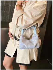 Close-up of light blue hobo bag with pleated strap and golden chain detail on shirt