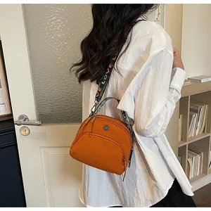 Detalle del bolso bandolera de nailon naranja con cremalleras y correa con letras