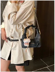Detail of grey denim crescent bag with pleated handle, chain strap, and plush charm