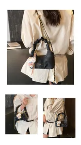 Detail of dark denim crossbody bag with gold chain strap and cute plush cat pendant