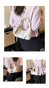 Detail of white crescent bag with ruched handle, gold chain and cat plush pendant