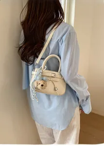 Detail showing creamy white crossbody bag with cute teddy pendant and blue bow accessory