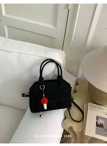 Detail of black suede handbag featuring a red mushroom charm and embossed MUTING logo