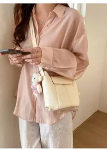 Detail of a chic cream bucket bag with a cute white teddy bear charm and vertical stitching