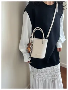 Detail view of cream white bucket bag with textured leather and a brown bear pendant