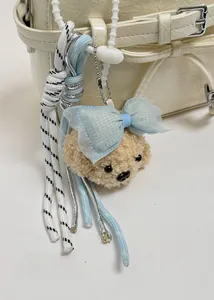Detail view of a cute beige plush bear charm with a blue bow on a white leather handbag